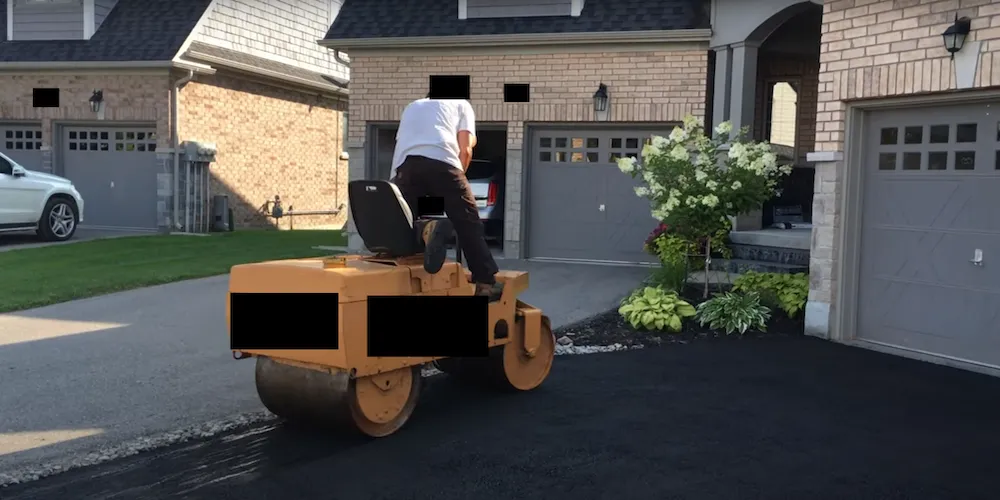 Un homme utilisant un camion compacteur pour compacter la surface en asphalte d'une entrée résidentielle