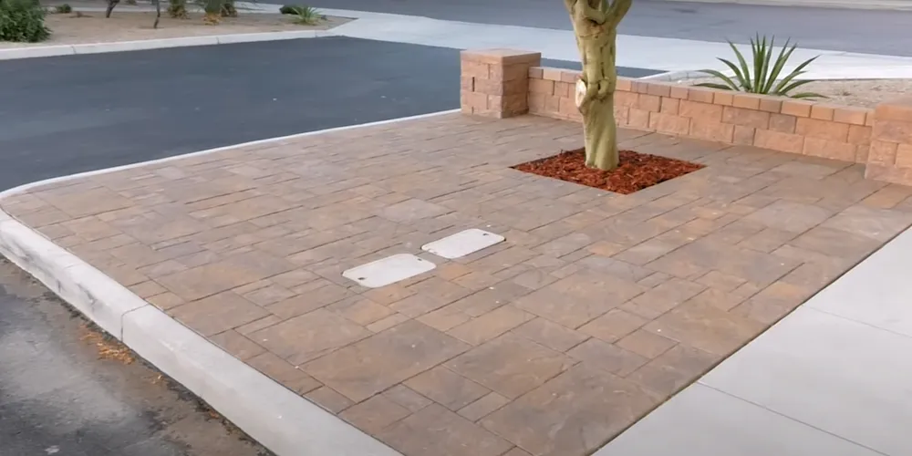 A sidewalk paved with red paver stones, with a tree visible along the path